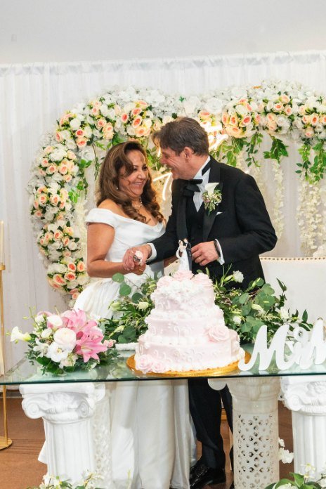 Los novios cortando el pastel bajo el arco de flores