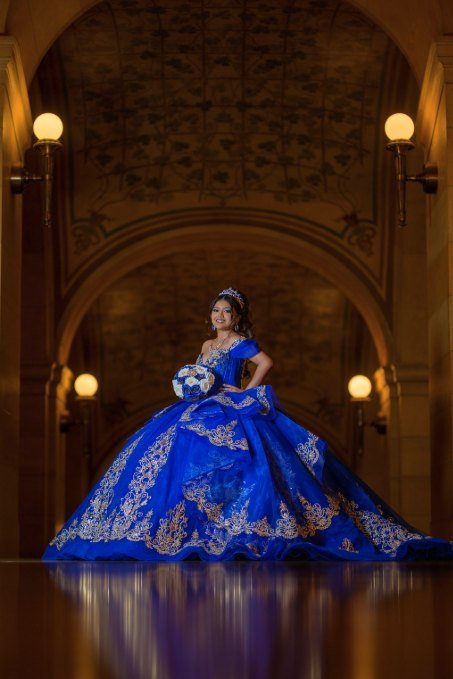 Quinceañera de pie bajo la arcada del salón, con el vestido azul extendido