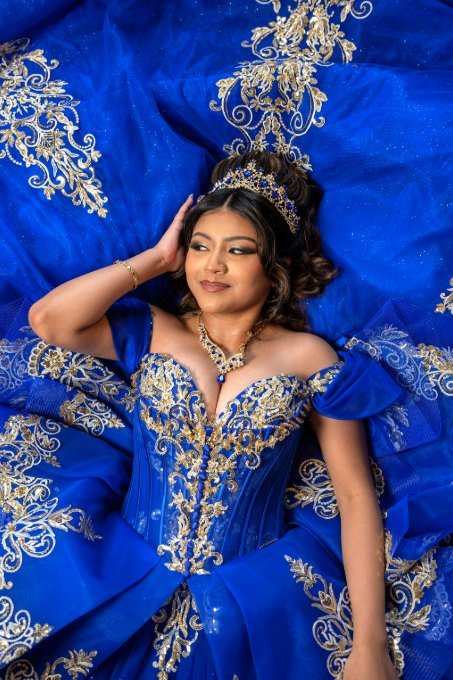 Quinceañera recostada, rodeada por el vuelo del vestido azul y dorado
